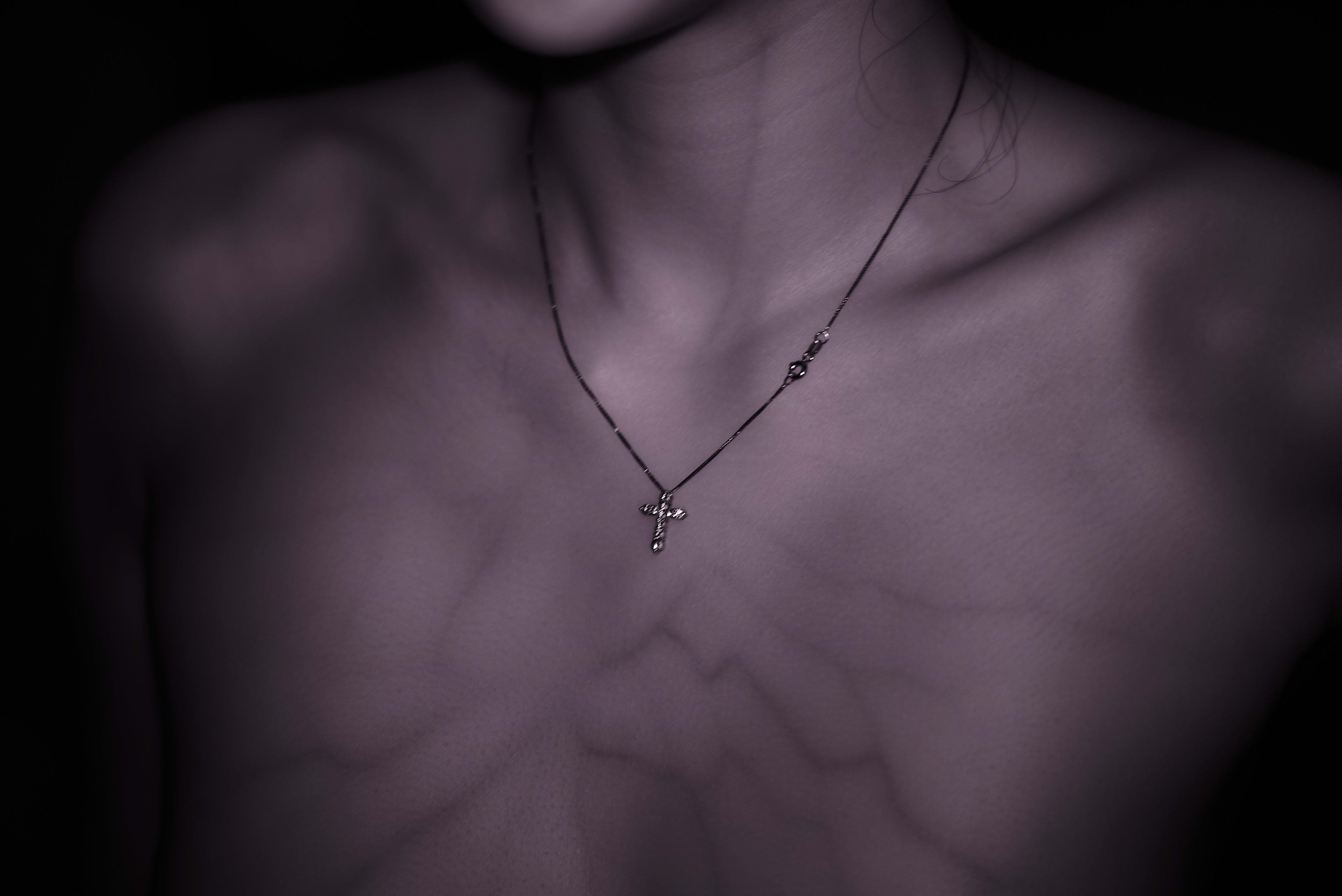 A close view of a neck, collarbones, and a cross pendant in hard shadow.