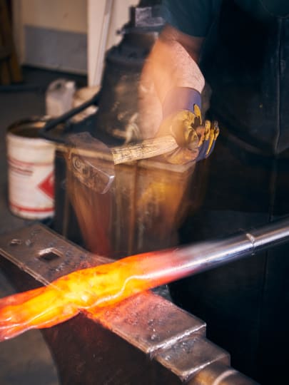 A blacksmith forges metal using a hammer and anvil. The image captures the intensity of the work with motion blur on the hammer.