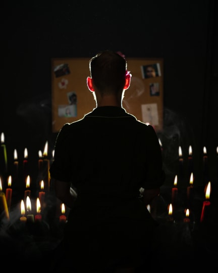 A figure stands in front of photos and candles.