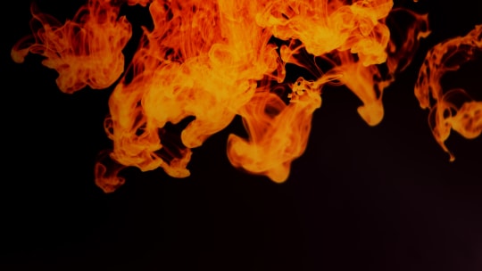 Abstract image of orange, swirling, smoke-like forms set against a black background. The forms evoke a sense of movement and energy.