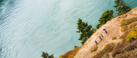 A group walks along a hillside above open water.