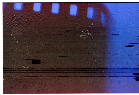 Old film stock scanned as an abstraction, with scratches, dust, red-brown tones, and blue light.