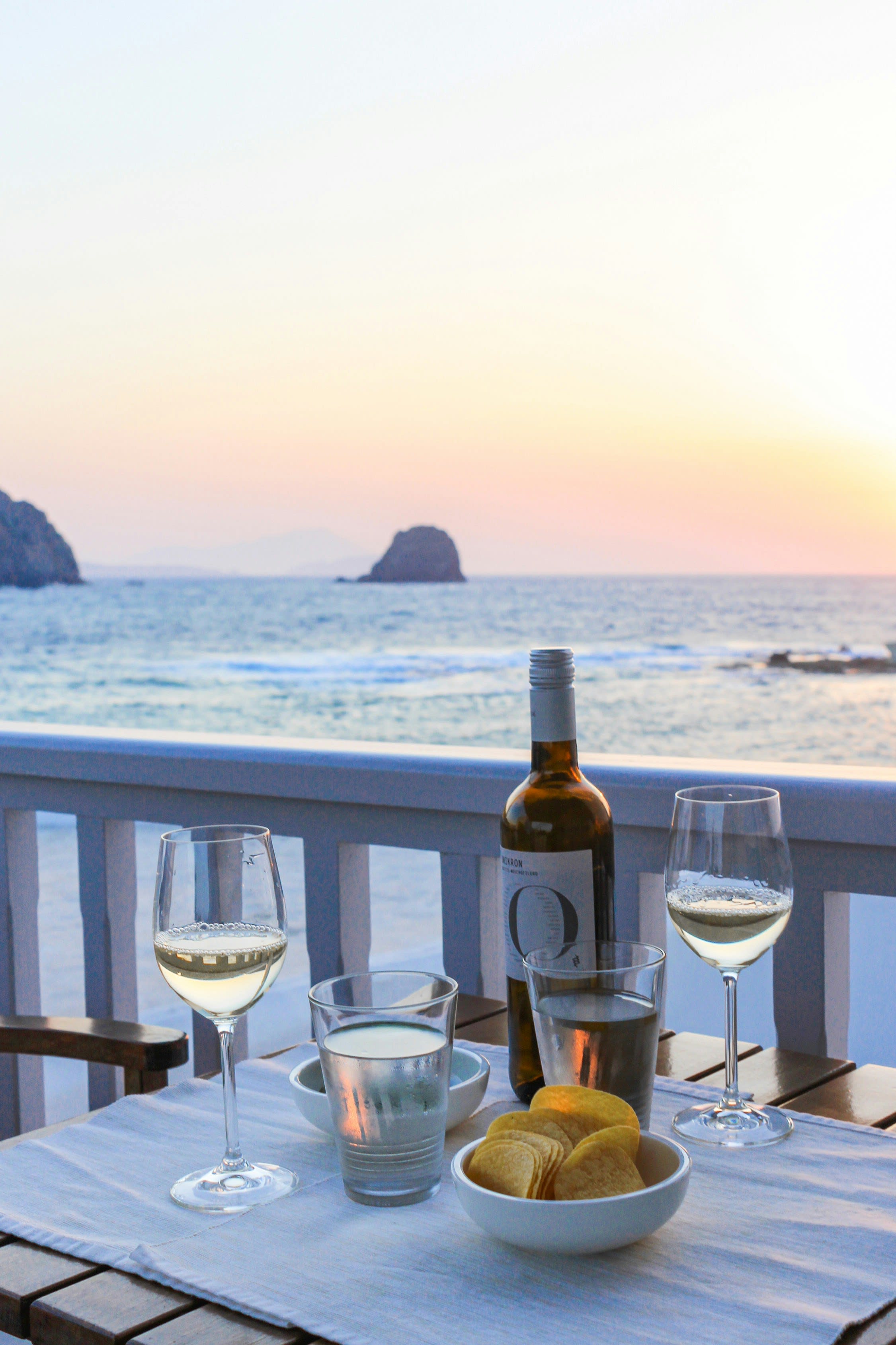 A couple at a caldera-edge table in Santorini at sunset, two glasses of wine