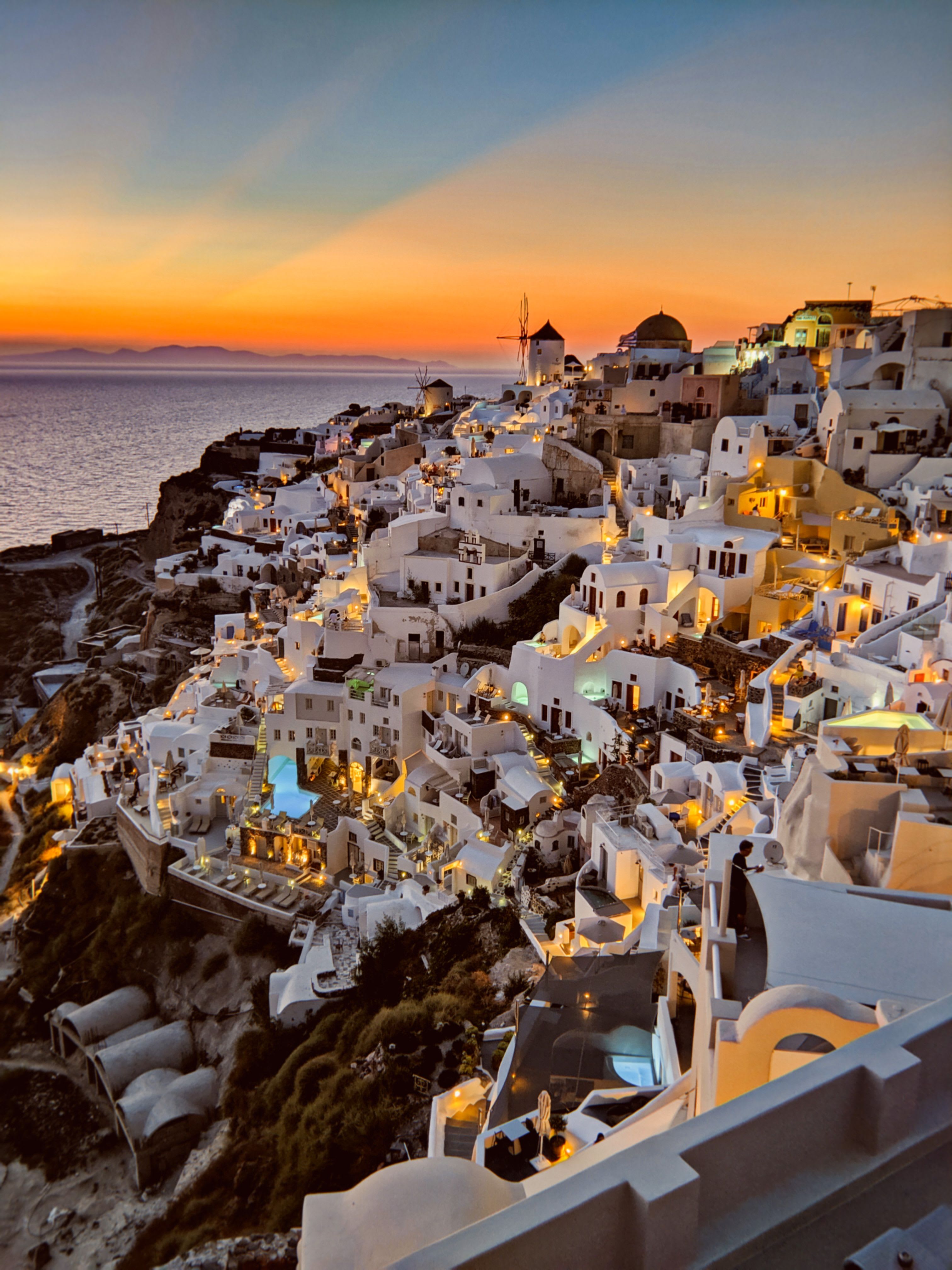 Caldera-edge hotels in Oia at golden hour, infinity pools above the sea