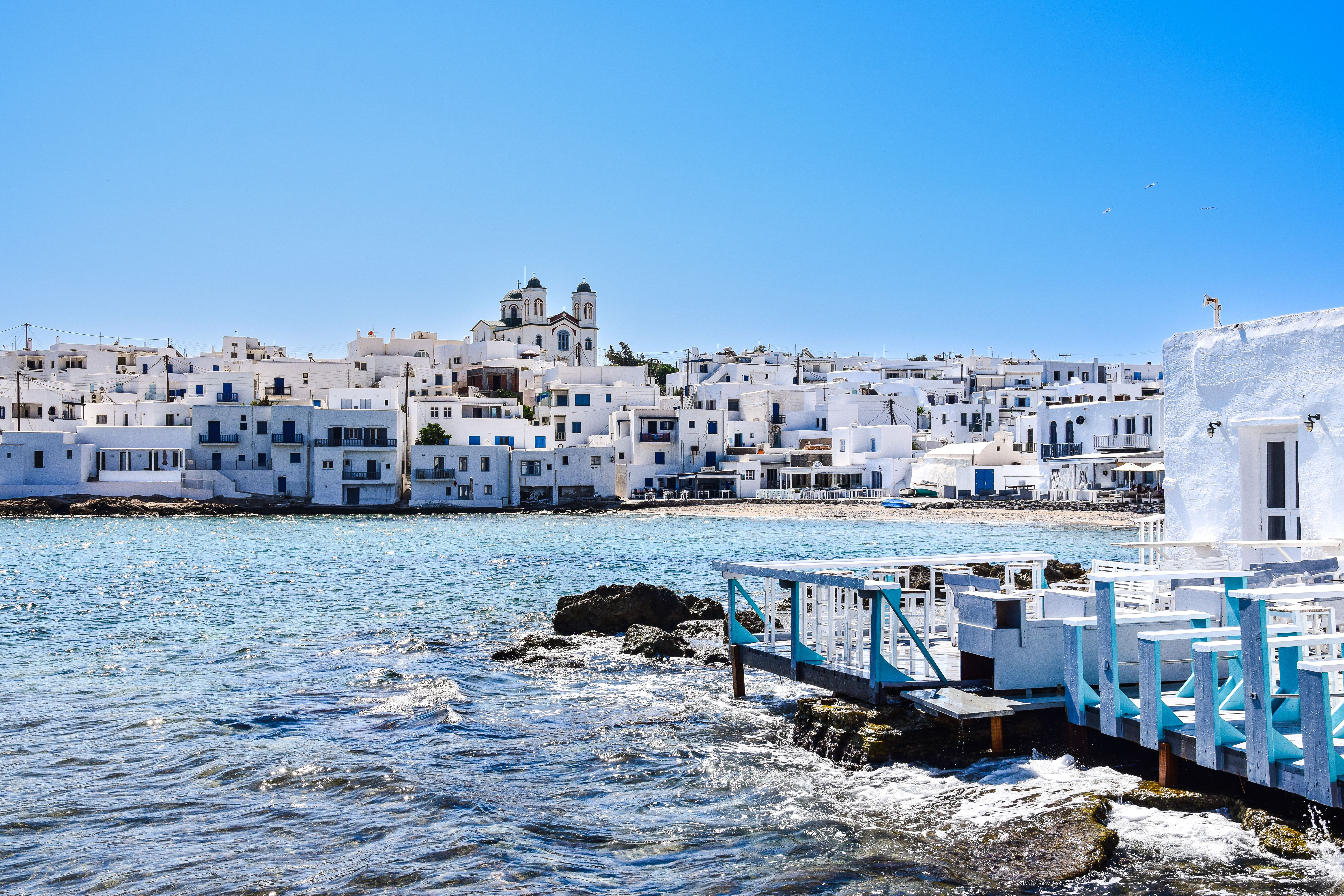 A montage-feel Cycladic scene — white villages, blue domes, turquoise sea