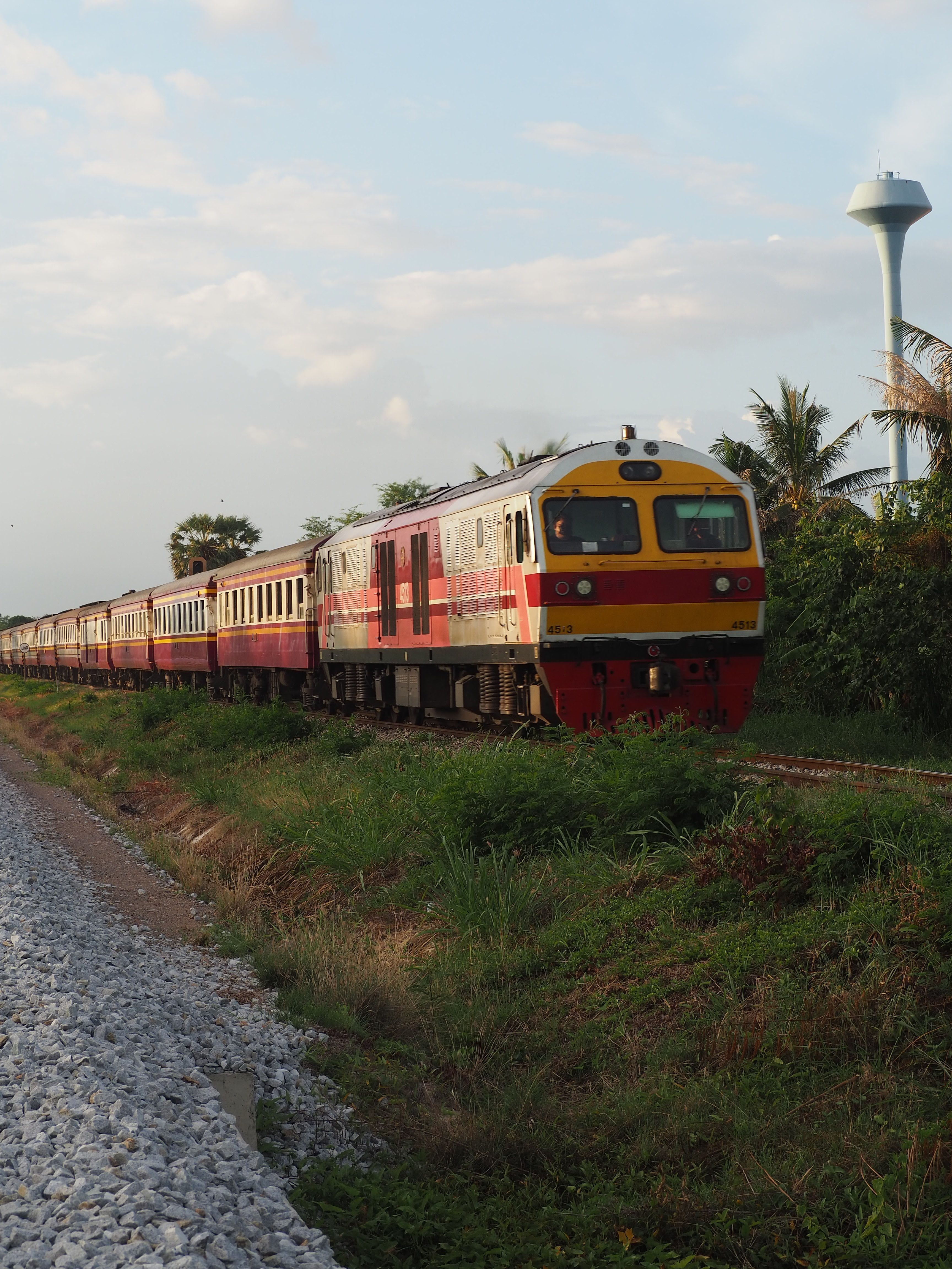A Thai train traveling through green rice fields and hills