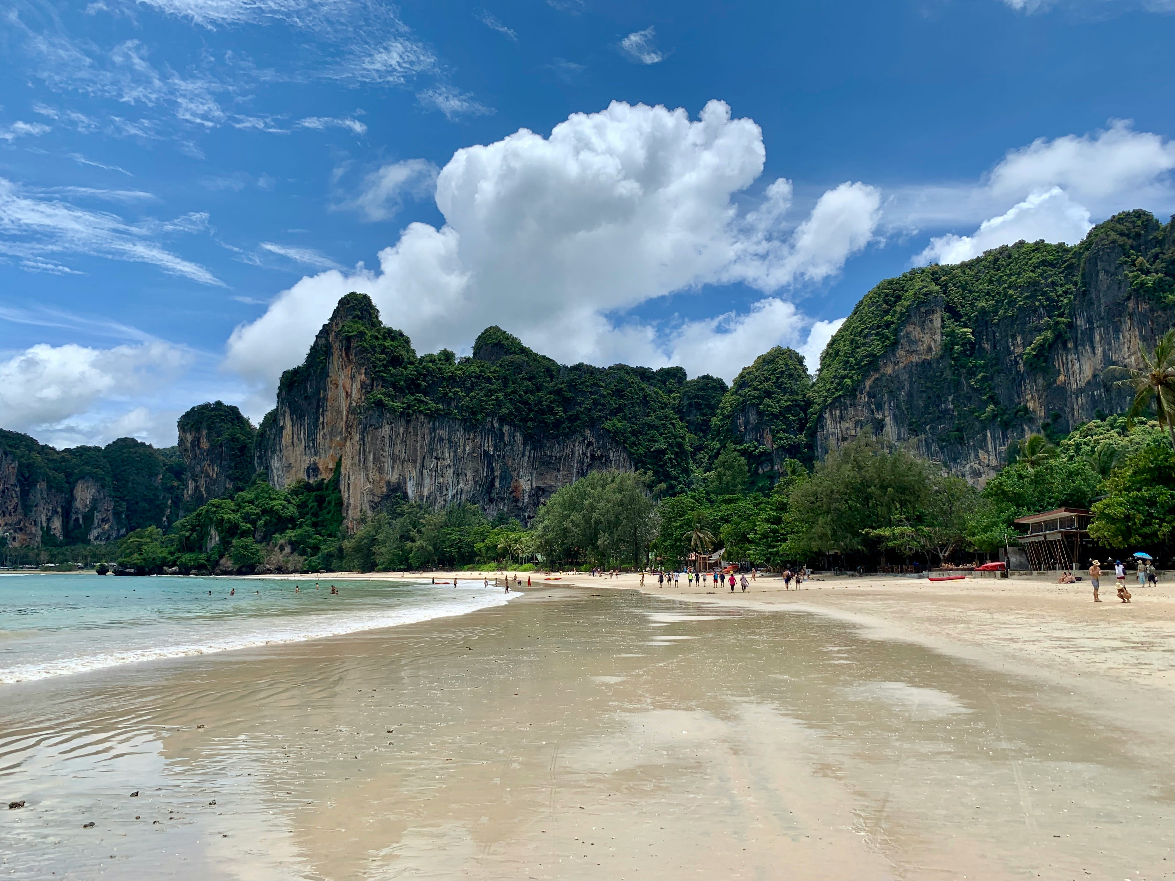 A quiet longtail-dotted beach with clear shallow water, fewer crowds