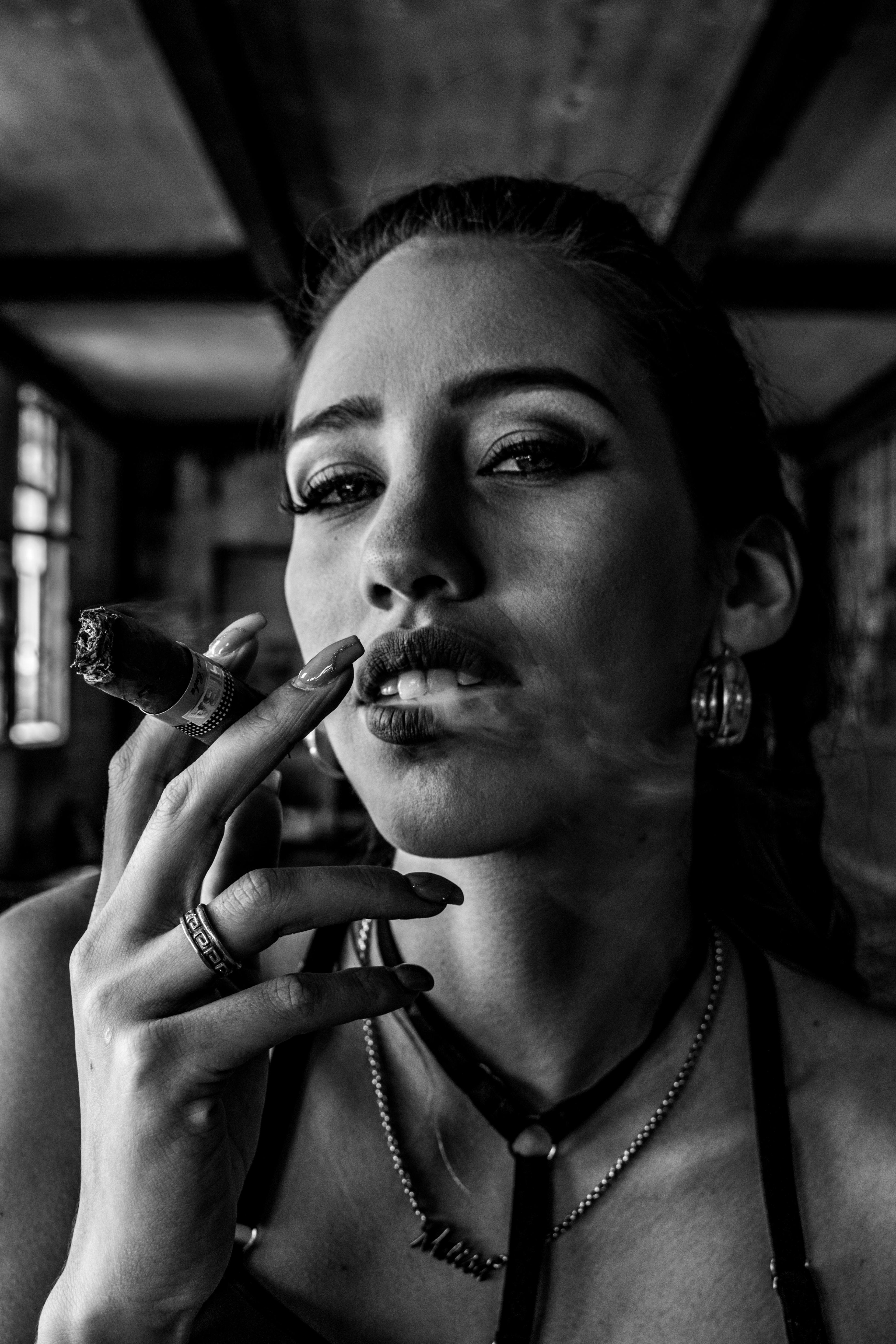 Retrato en blanco y negro de una mujer fumando un puro con actitud desafiante y segura, destacando detalles de joyería. Arte boudoir y empoderamiento femenino por Vanguardia.