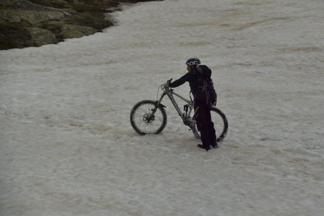 A cyclist pushing his bike through the alpine snow