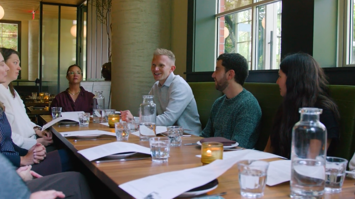 Group gathered around a table in warm conversation, part of an AI Mental Health Collective gathering