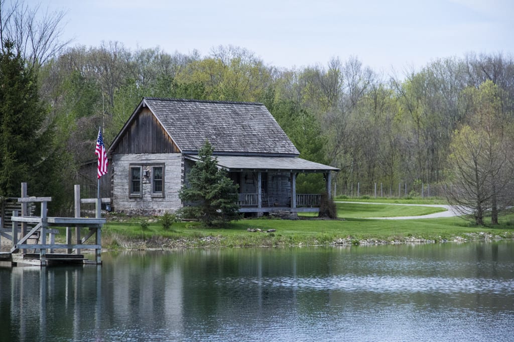 The historic log cabin with an American flag, reflected in the pond