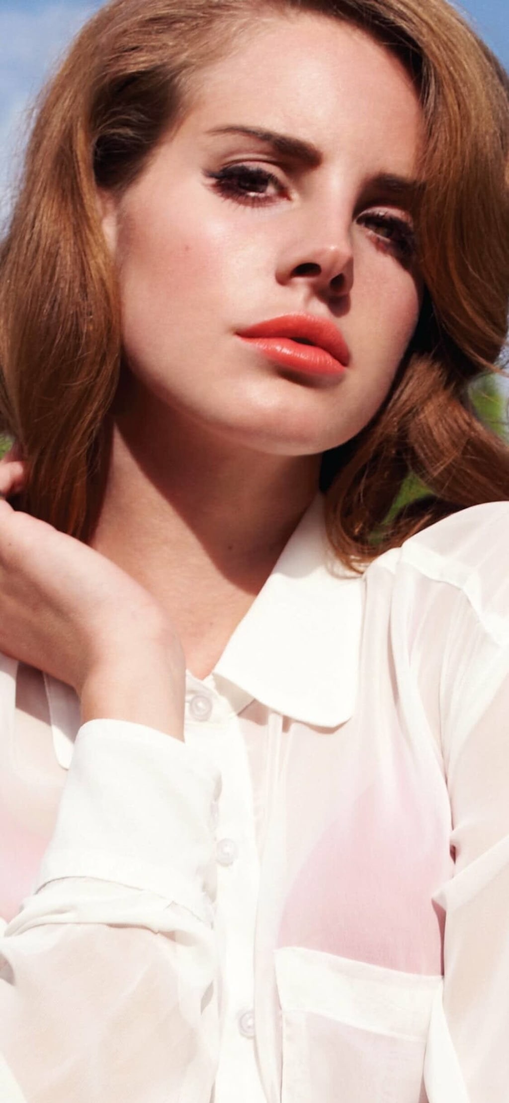 Portrait of woman with auburn hair wearing white shirt, looking thoughtfully downward with soft makeup against blue sky backg