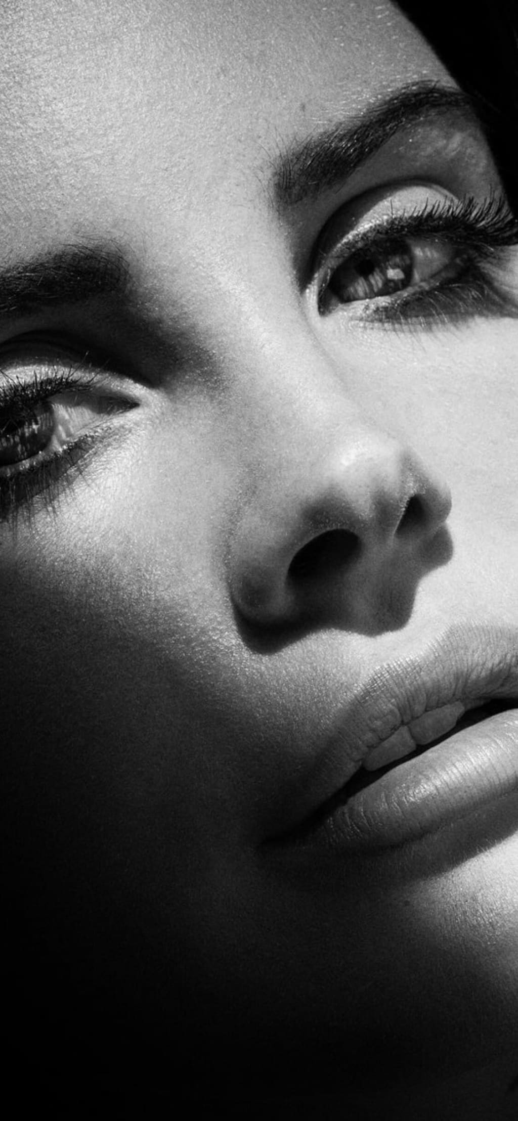 Black and white close-up portrait of a woman with dramatic eye makeup, bold brows, and defined facial features in artistic st