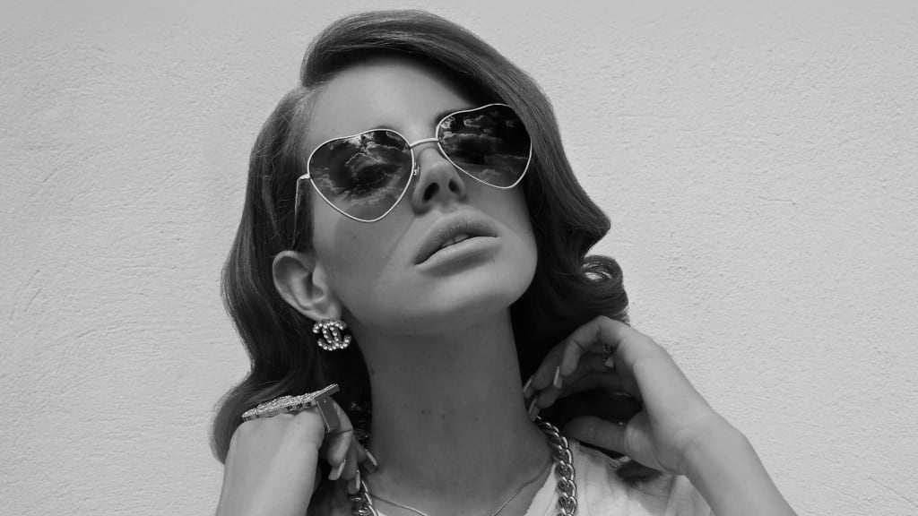 Black and white portrait of woman wearing heart-shaped sunglasses and pearl jewelry with styled dark hair against neutral bac