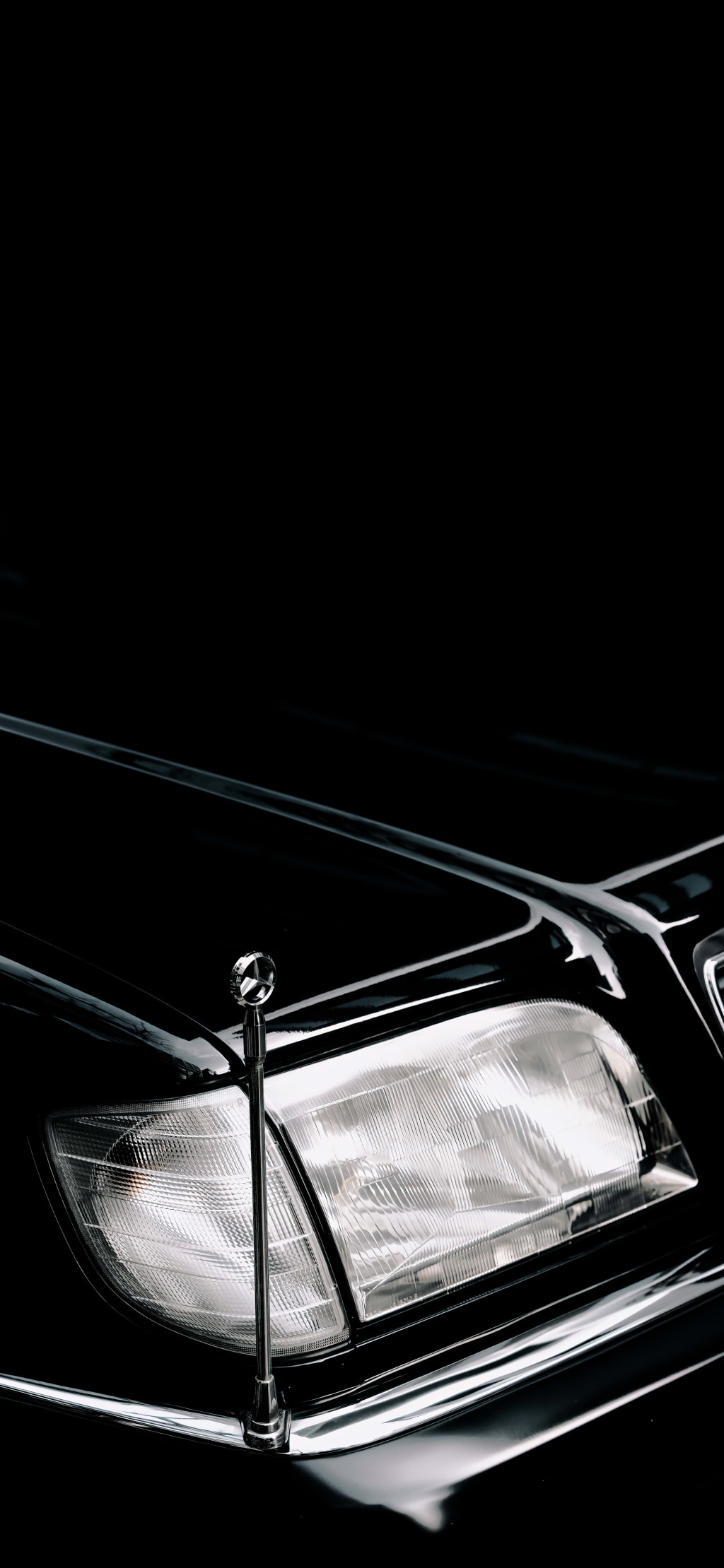 Close-up of a classic car's chrome headlight and front grille against a dark background, showcasing vintage automotive design
