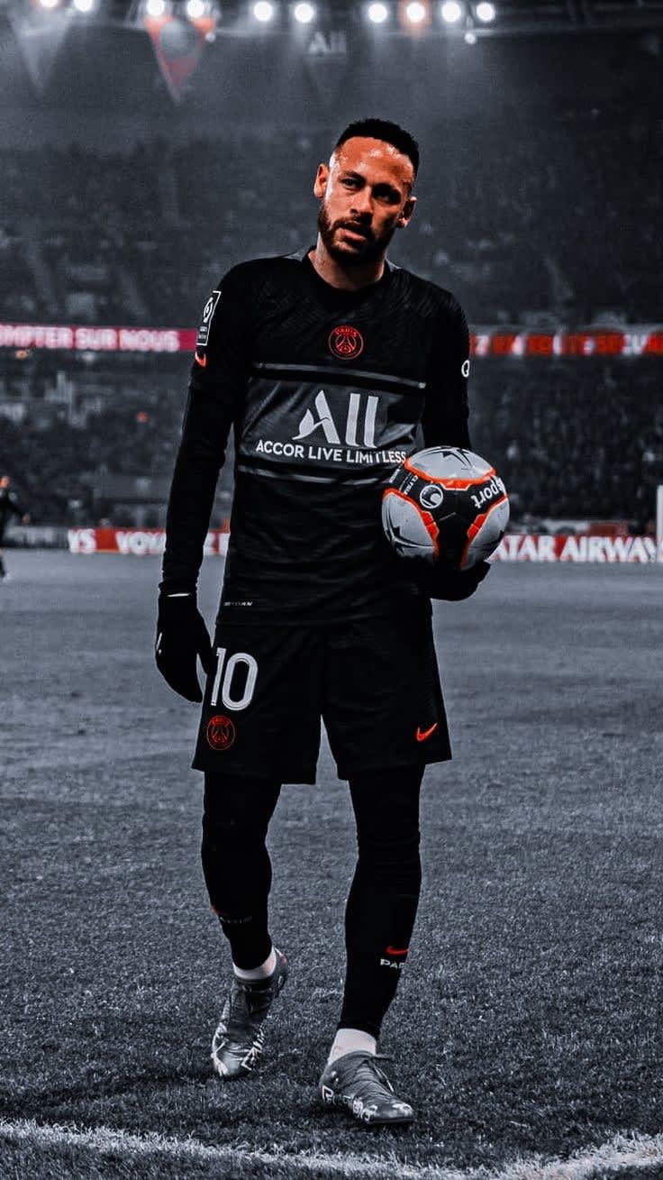 Professional football player wearing black jersey with number 10, holding soccer ball on stadium field with crowd in backgrou