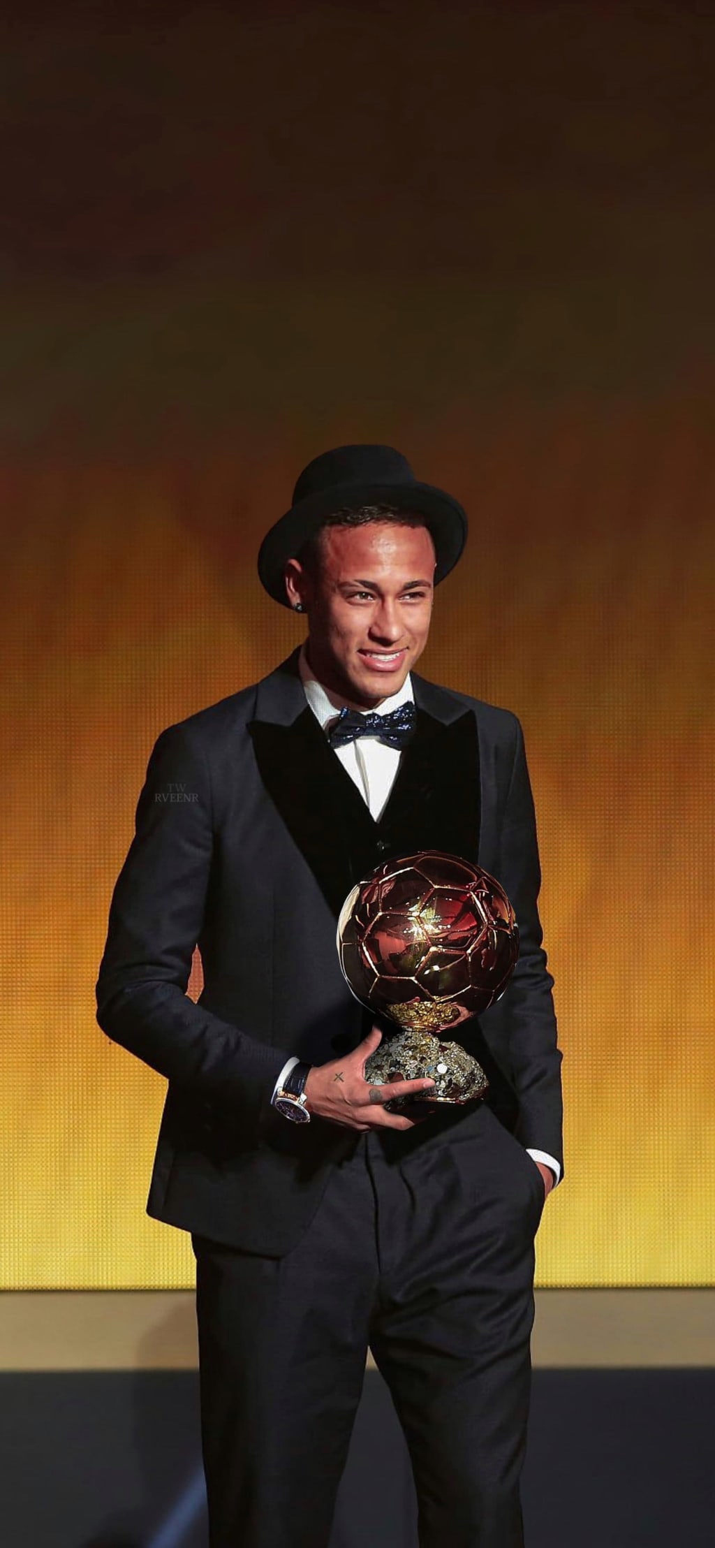 Stylish athlete in black tuxedo and fedora hat holding a golden award trophy against warm gradient background