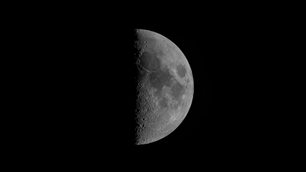 Half-illuminated moon showing detailed craters and surface texture against a deep black starless sky, captured in high-resolu