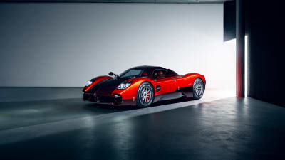 Striking red sports car with black racing stripes parked in a modern minimalist garage with concrete floor and industrial lig
