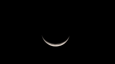 Delicate crescent moon illuminated against a deep black night sky, showing subtle surface details and earthshine