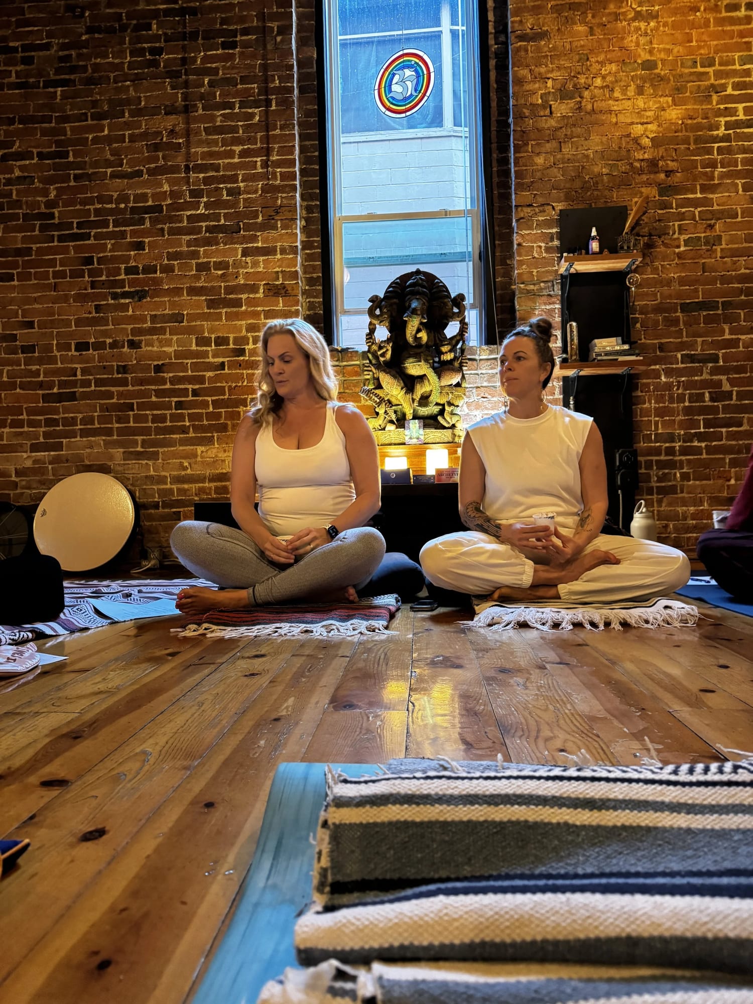 Becky and Andrea sitting in meditation at a yoga studio