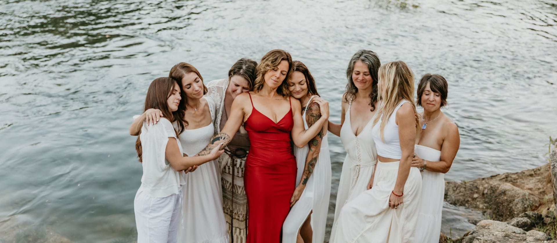Andrea in red with a circle of women gathered around her by the river