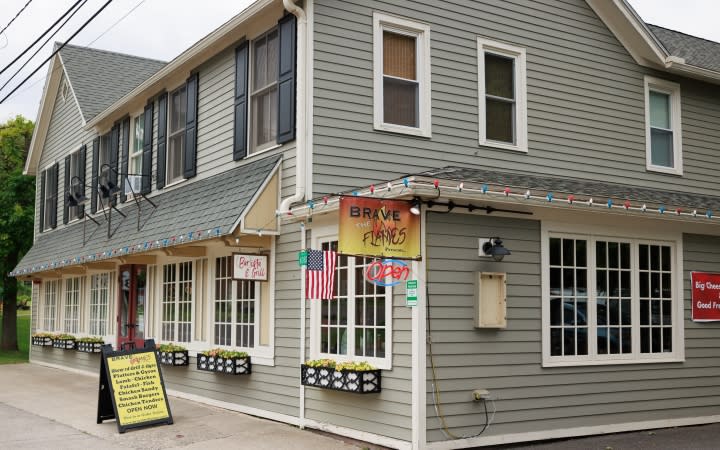 A two-story gray commercial building with storefronts and signage on a tree-lined street in Greene County.
