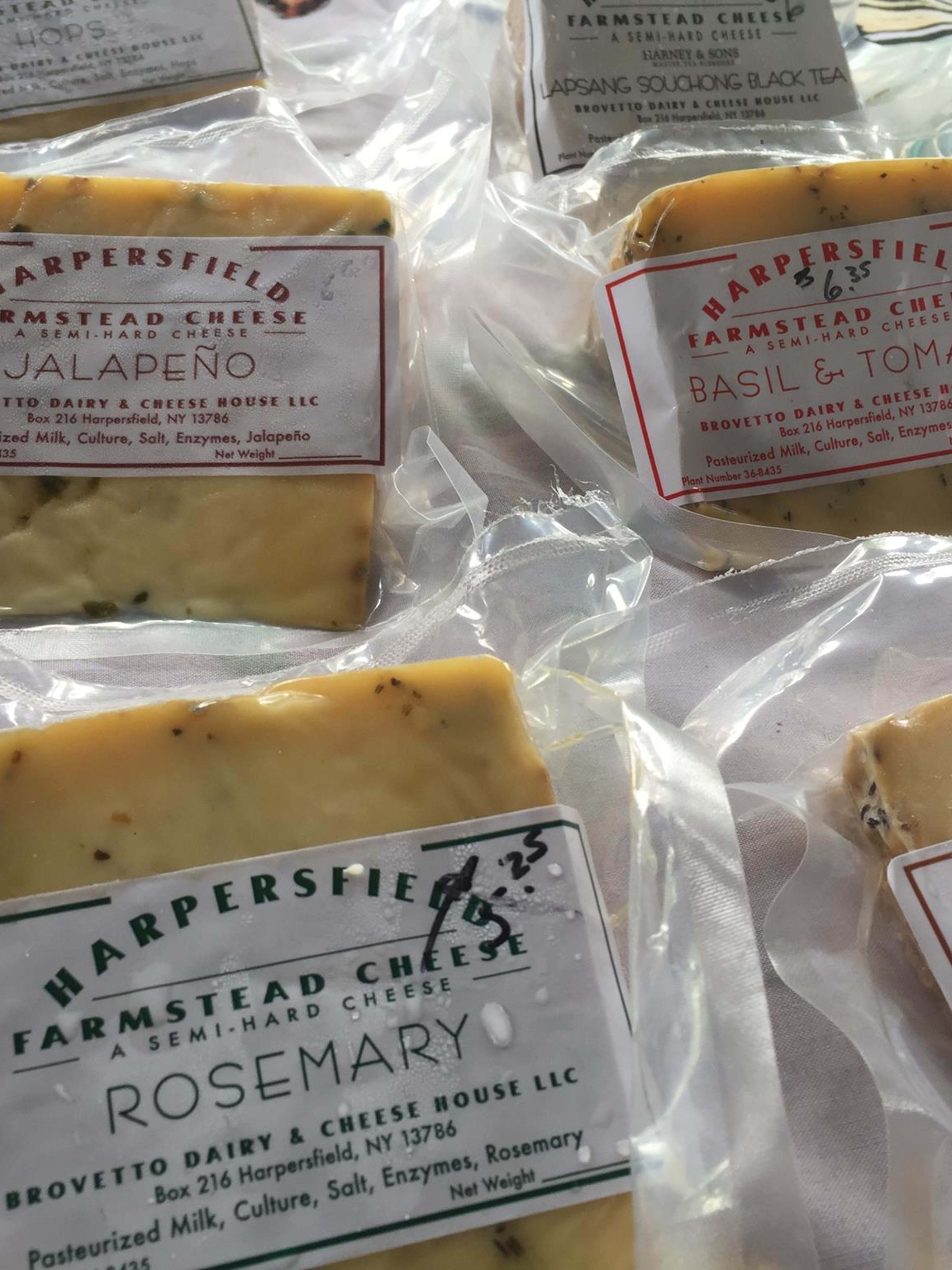 Packaged farmstead cheeses from Harpersfield and Brovetto Dairy displayed with flavor varieties including Jalapeno, Basil & Tomato, Rosemary, and Caraway.