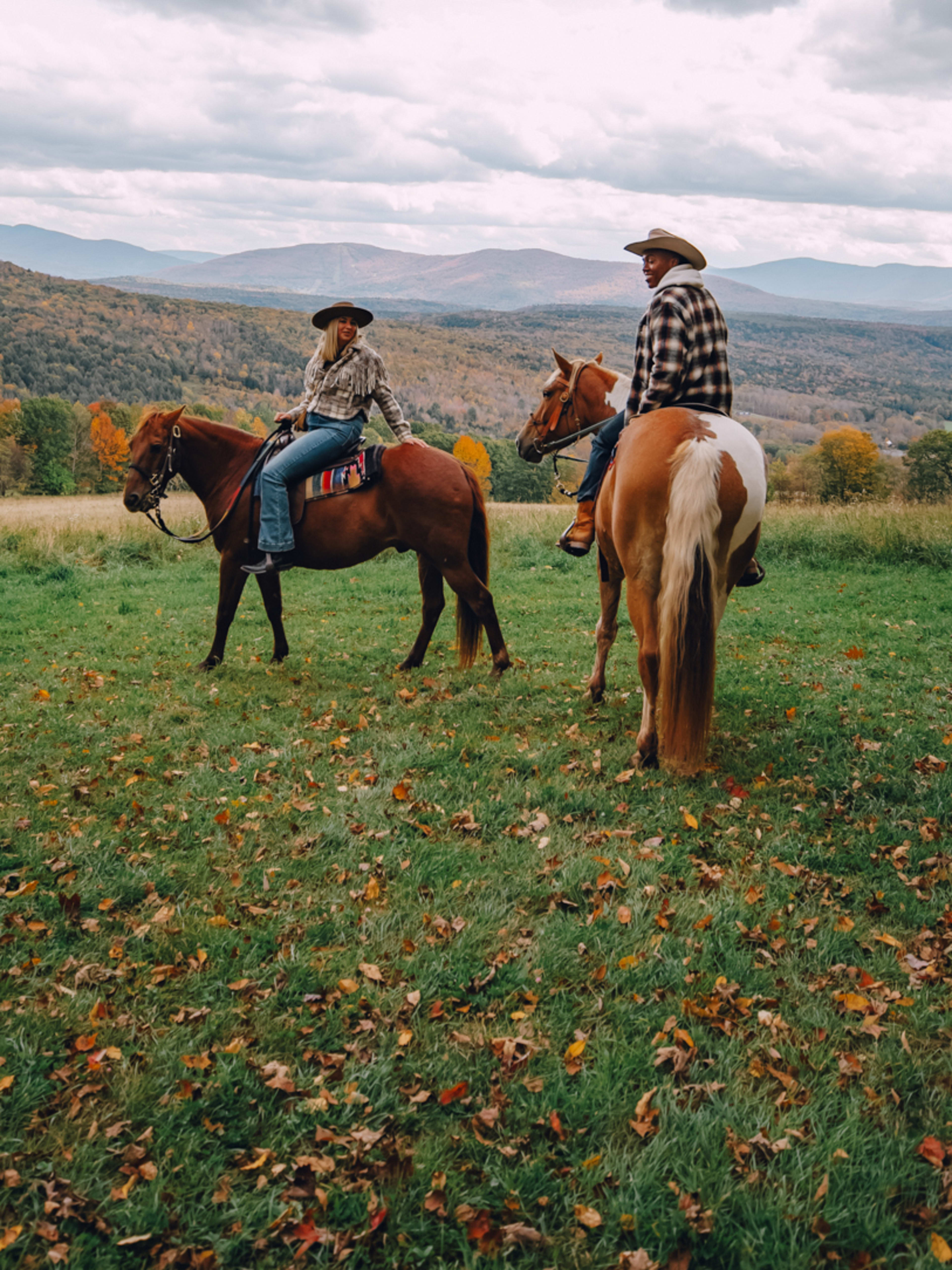 Two cowboys on horseback in a autumn meadow with Catskill Mountains in the background.