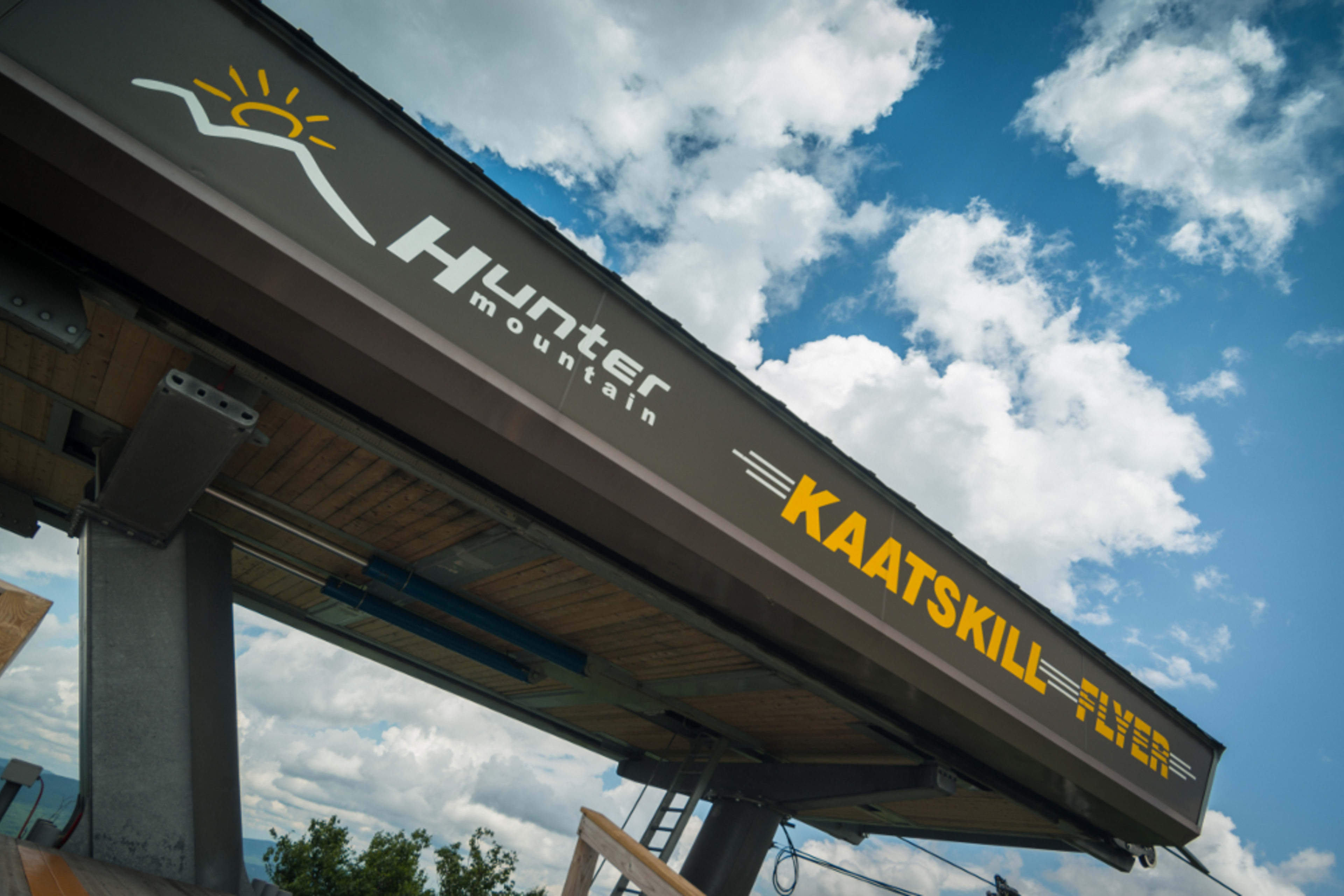 Hunter Mountain Kaatskill Skyride sign on overhead structure against blue sky with clouds.