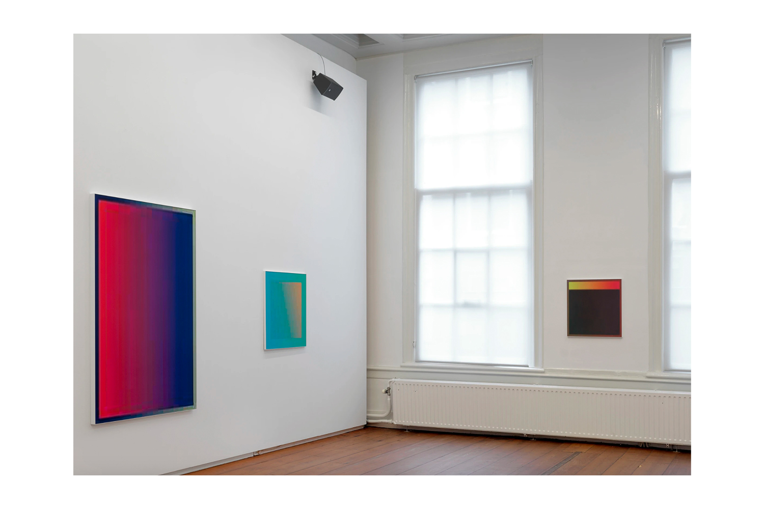 Three color gradient works on white gallery walls beside tall windows