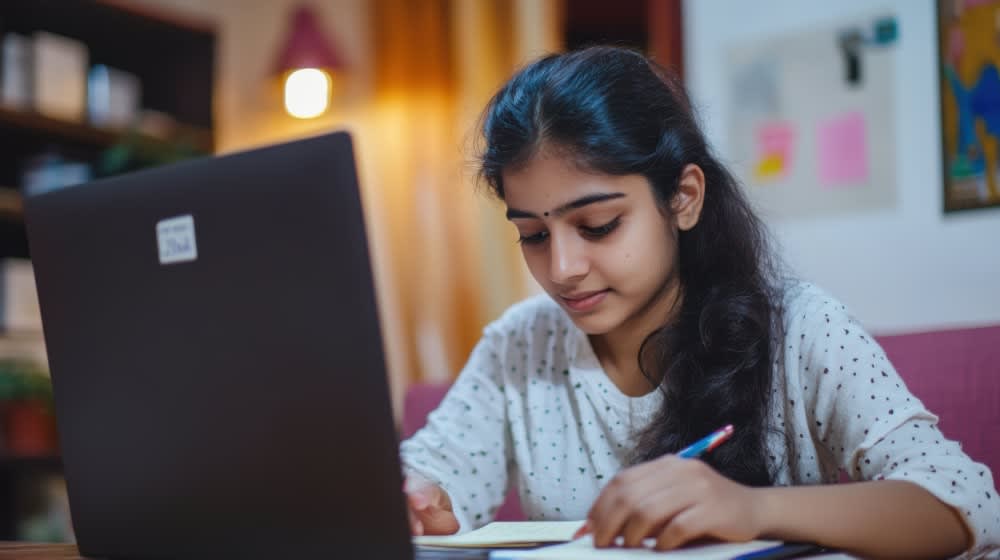 indian-teenage-girl-engaged-online-learning-home-using-computer-taking-notes