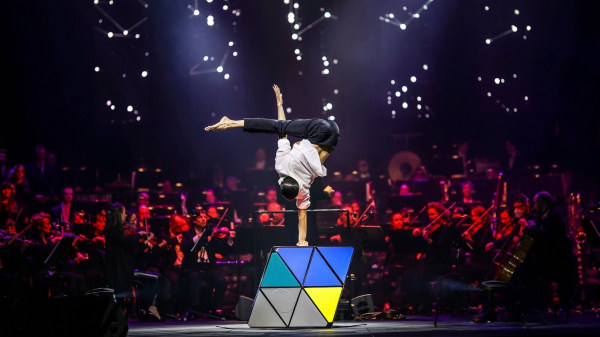 Artist performing a handstand on a overdimensional rubik cube infront of an audience