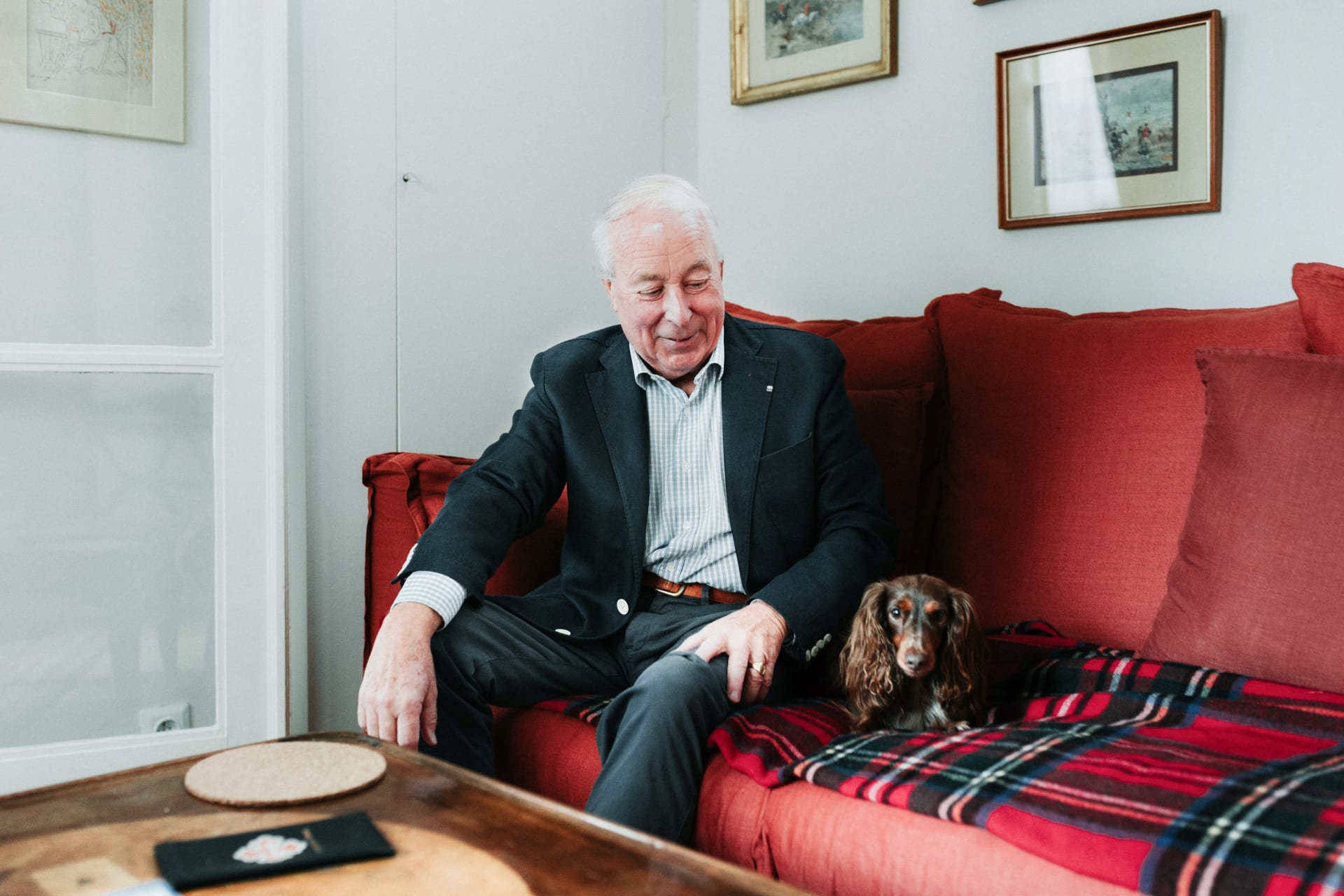 Personne âgée assise sur un canapé rouge avec son chien.