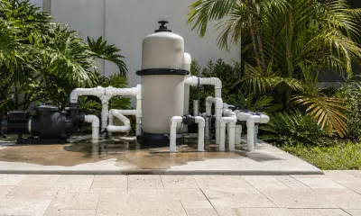 Pool equipment pad with a pump, filter tank, and valves standing in a spreading puddle of water on the concrete slab