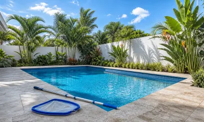 Skimmer net on a telescopic pole resting on the paver deck beside a clean blue Miami backyard pool