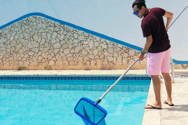 Pool technician skimming a crystal-clear pool ready for summer in Miami