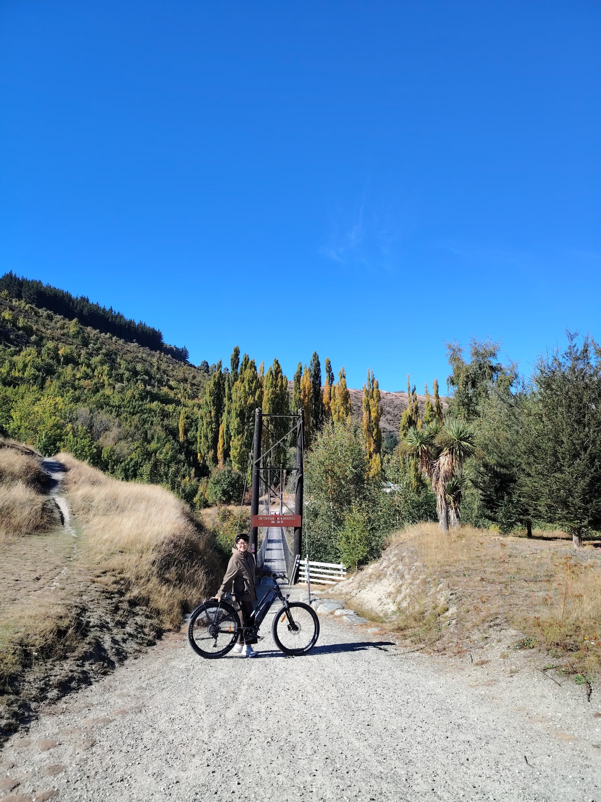 Customer pausing on the trail with the Gibbston hills and a swing bridge ahead