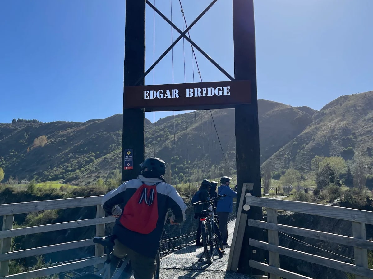 Customer beaming on a long suspension bridge with the Gibbston hills behind