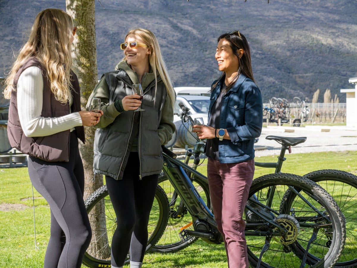 Three friends laughing over a glass of wine beside their parked Whizzy e-bikes