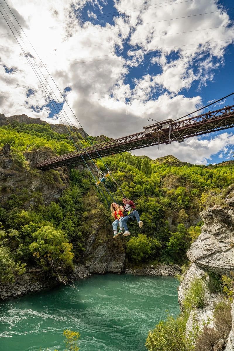 Two riders on the Kawarau Swing beneath the historic AJ Hackett bungy bridge over the Kawarau River, Queenstown