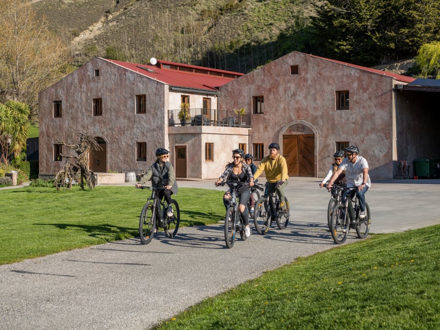 Group of cyclists arriving on Whizzy e-bikes at a stone-walled Gibbston Valley winery