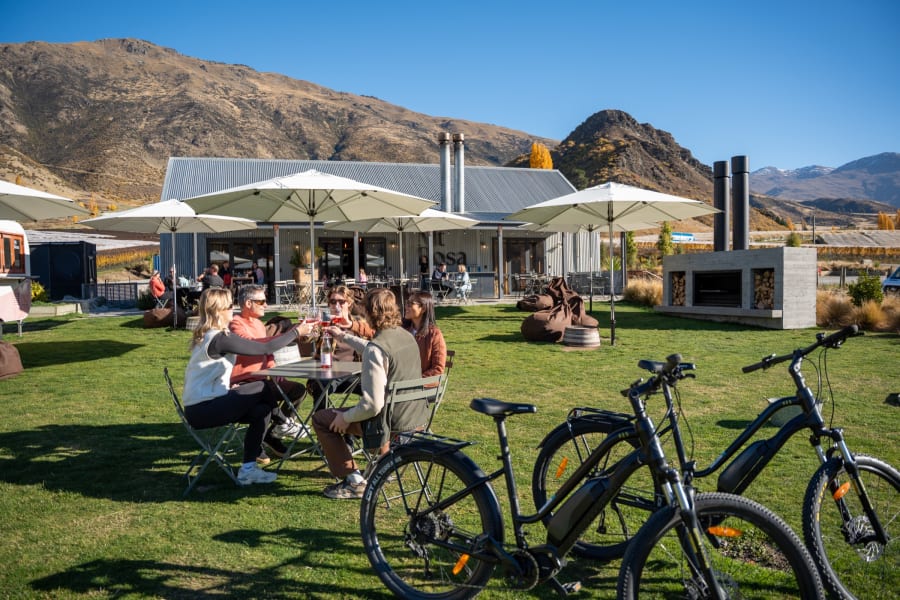 Group of friends toasting glasses of rosé on the lawn at Mt Rosa winery in Gibbston Valley with their Whizzy e-bikes parked beside them