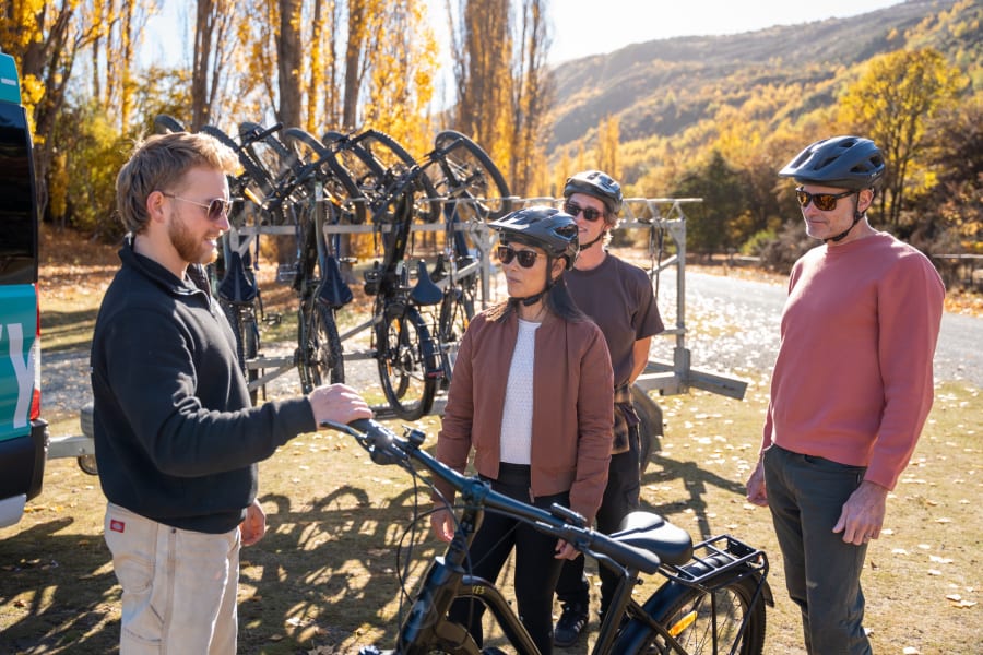 Whizzy guide briefing customers and fitting helmets beside the e-bike rack with autumn poplars behind