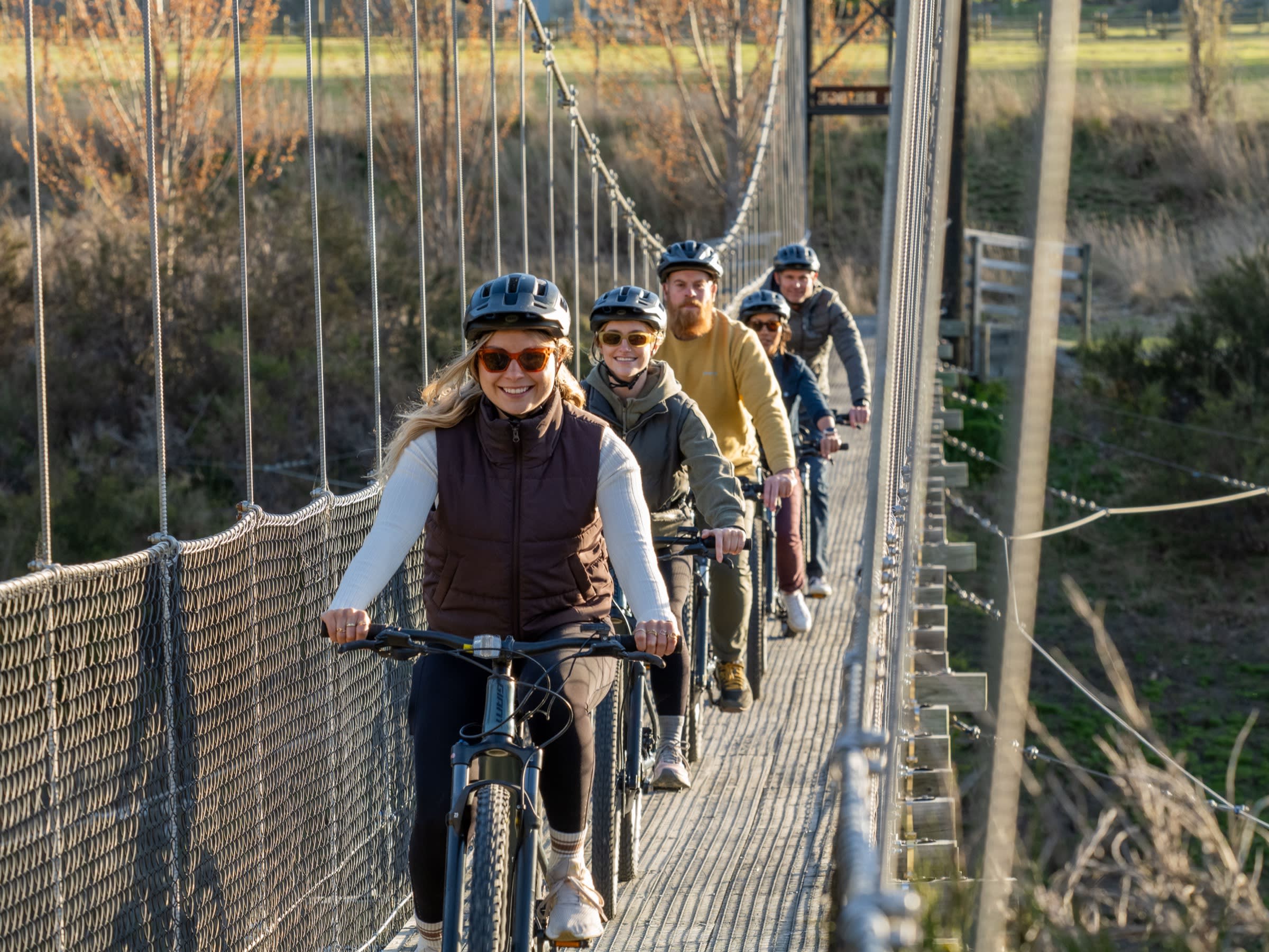 Group of e-bike riders crossing the Edgar Suspension Bridge with the trail and willows behind