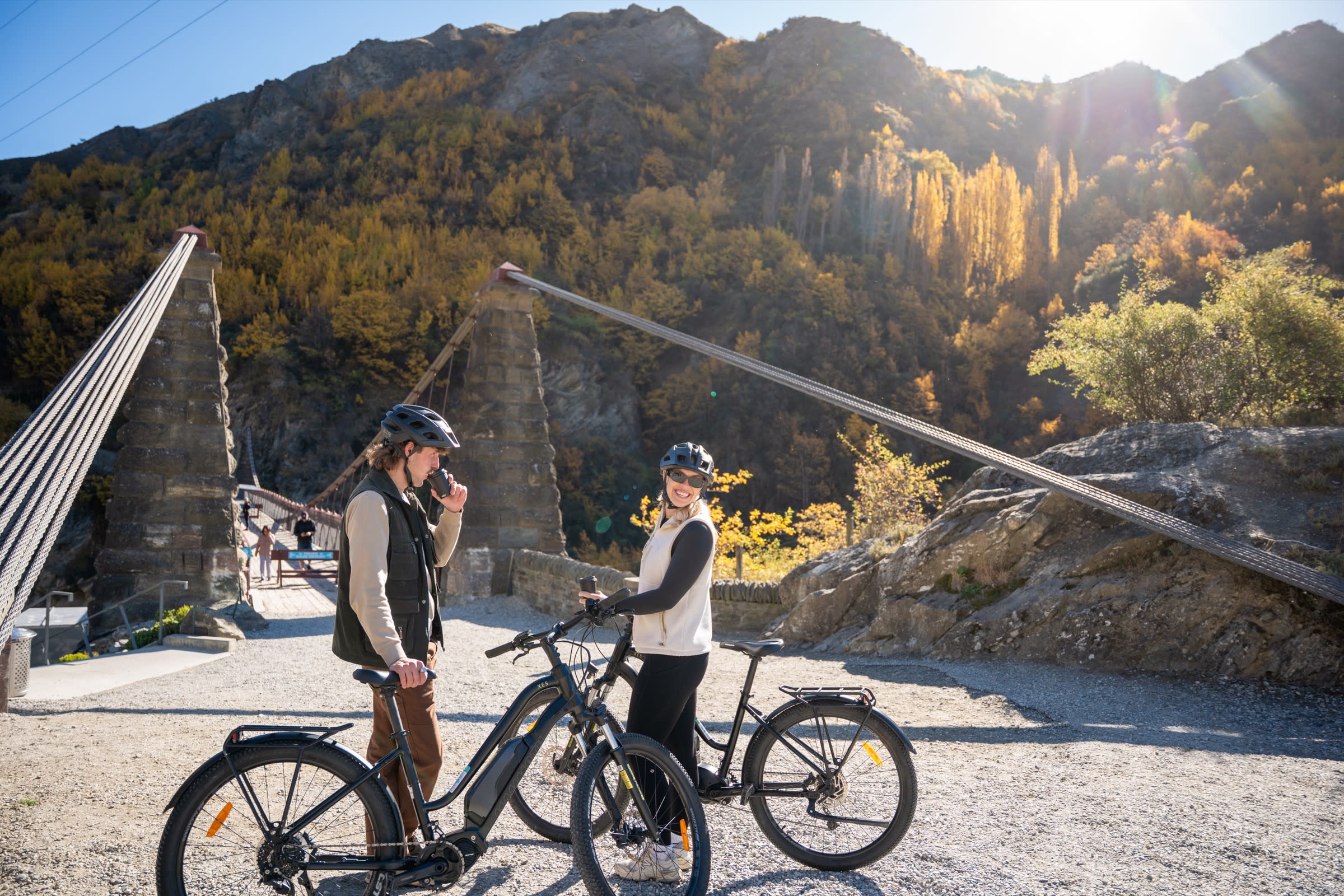 Couple pausing for a coffee at the historic 1880 Kawarau Suspension Bridge with autumn poplars behind