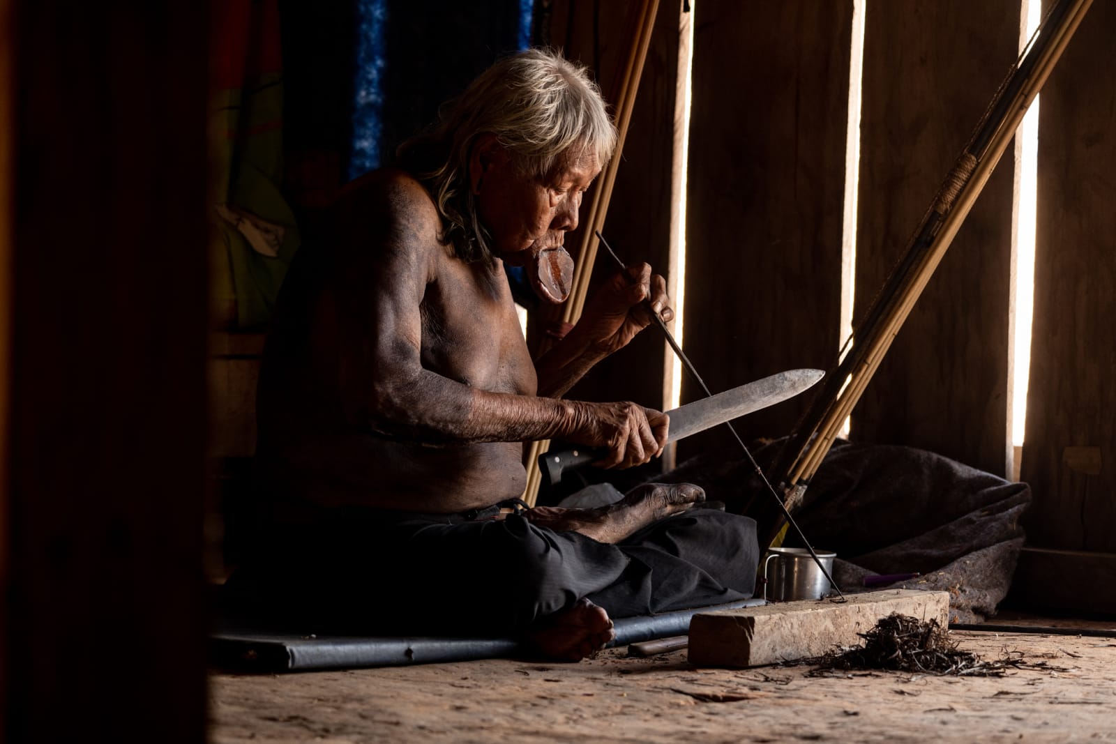 Chief Raoni sitting on the floor of his house making arrows