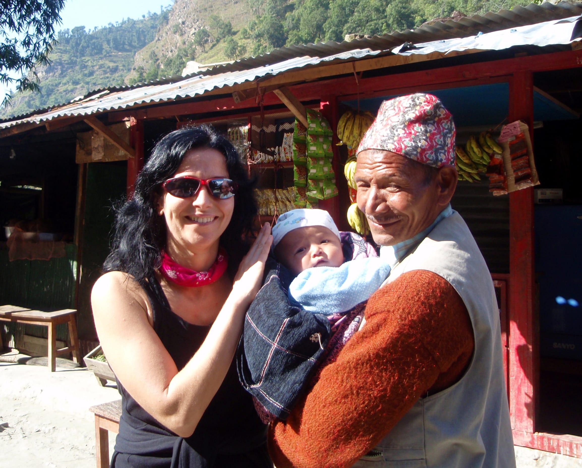 Magda Kapela z uśmiechem pozuje z lokalnym mieszkańcem Nepalu, trzymającym dziecko w tradycyjnym ubraniu.