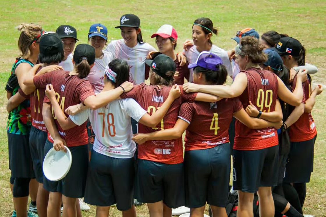 Woman's frisbee team circles up in a huddle on the field.