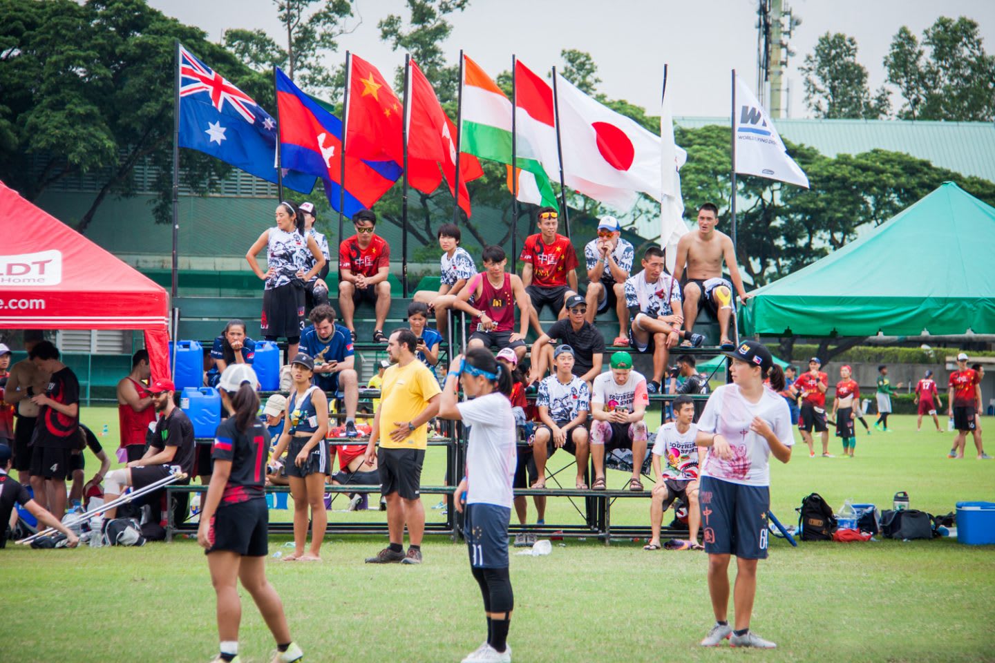 Chinese female ultimate frisbee athletes compete in a tournament with international flags flying in the background of the bleacher seating.